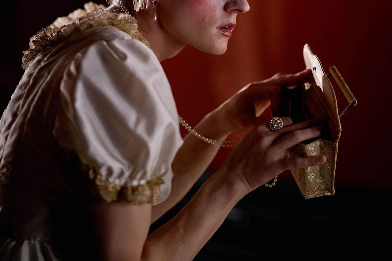 A woman in vintage attire carefully opens a purse, highlighted by moody lighting.